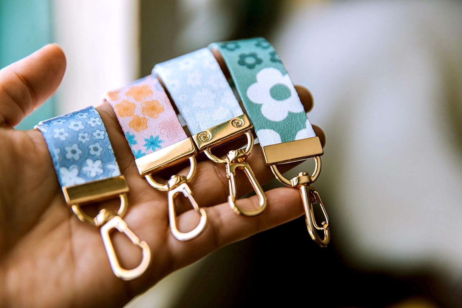 May include: Four keychains with gold metal clasps and fabric straps with different floral patterns. The straps are blue, pink, light blue, and green.